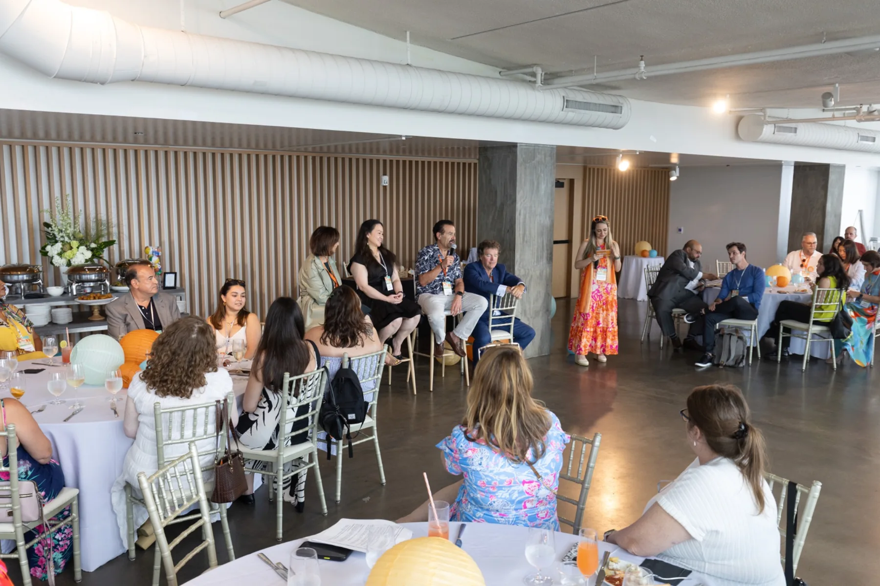 Attendees gather at round tables while a speaker addresses guests at a corporate event